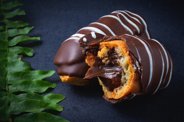 Chocolate bomb. Traditional Brazilian eclair bitten with apparent filling on a black background and branch of leaves. 