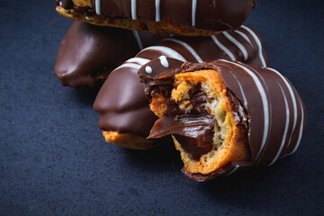 Chocolate bomb. Traditional Brazilian eclair bitten with apparent filling on a black background and branch of leaves. 