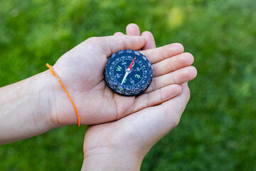 Girl holding the compass. Hands of a teenager girl holding a liquid compass. Green grass...
