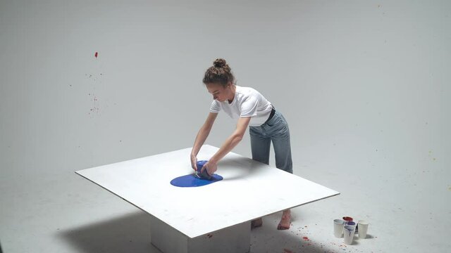 Female artist draws by pouring paint on the canvas, a talented artist draws a color blue abstraction, pouring of paint on canvas, experimental painting.