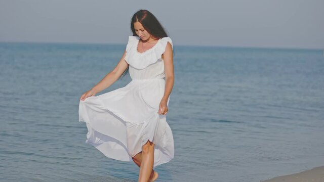 a woman in a white dress walks barefoot on the sea