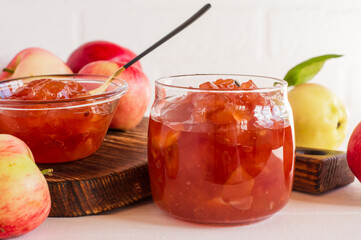 transparent apple jam is delicious and beautiful in a glass jar close-up against a white brick wall.