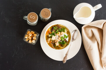 seasonal summer soup of forest mushrooms with cream, greens and croutons. delicious lunch. black background. top view.