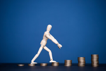 Stacks of golden coins like income graph and wooden man walking.