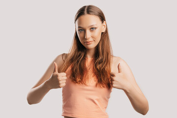 Beautiful young girl smiling and shows thumbs up gesture with two hands on a white isolated background. Positive woman points to an idea, a place for advertising