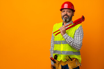 Middle-aged bearded man builder in uniform and hardhat with tools against orange background