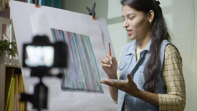 Young girl artist teaching canvas painting by recording on camera - concept of online teaching, virtual class or education during coronavirus, covid-19 pandemic