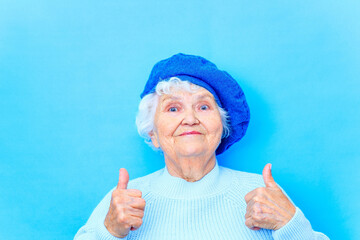 beautiful retired woman in blue beret and warm pullover looking at camera and smile in blue wall...