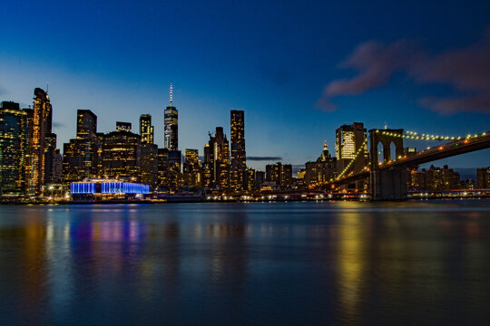 Stupenda vista notturna dello skyline di New York dal Brooklyn Bridge Park , Manhattan, New York. Fiume con palazzi illuminati come sfondo. Foto Panoramica in lunga esposizione.