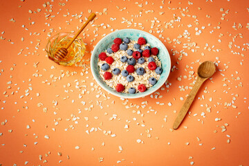 Healthy breakfast - oatmeal with blueberries and raspberries on orange background. Flat lay
