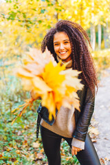 Young beautiful woman with a bouquet of yellow autumn leaves in the park on a warm autumn day