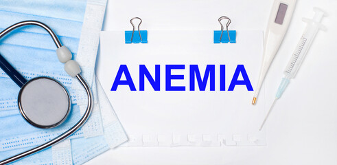 On a light background lie a stethoscope, an electronic thermometer, a syringe, a face mask and a...