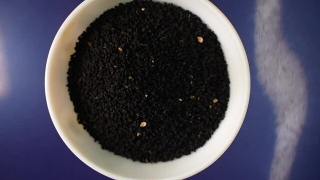 Some black cumin seed grains on a clay bowl on top of blue background slowly moving 