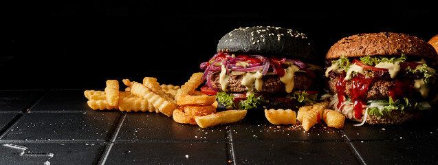 Appetizing burgers and fries on dark table in studio