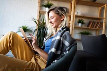 Relaxed young woman in sofa smiling content, happy and reading, working on tablet pc at home