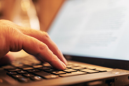 Eine Hand auf der Tastatur eines Laptops mit Bildschirm im Hintergrund
