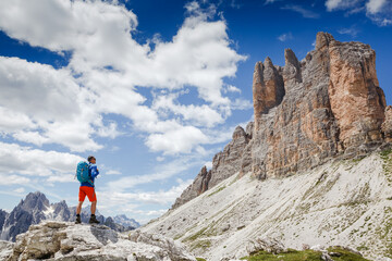 Naklejka premium Traveler Man with backpack standing on edge of cliff and looking at the mountains. National Park Tre Cime di Lavaredo, Dolomites Mountains, Italy