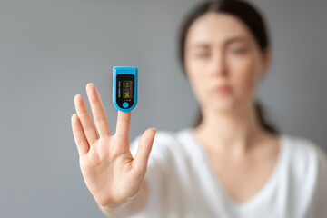 A woman shows her hand with a pulse oximeter on her index finger. Blurred portrait. Blue background. The concept of measuring oxygen in the blood