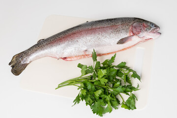 river trout and a bunch of greens lie on a white cutting board