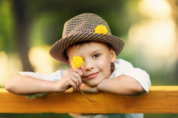 Portrait of happy boy in the hat. Child is smiling in spring day. Kid is enjoying spring. Sunny day. Boy holding dandelion. Outdoor, close up.