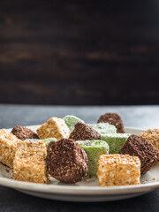 The traditional multi-colored oriental dessert Turkish delight (rahat locum) lies on a white plate against a gray background. Copy space. Side view