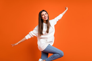 Fototapeta na wymiar Portrait of attractive cheerful girl having fun flying like plane fooling isolated over bright orange color background