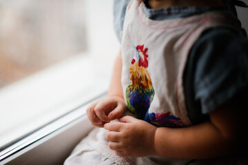 Sleepy toddler girl child in a dress near the window in a dark room, children's safety in apartments, a cozy photo in a dark interior, child play with curtains