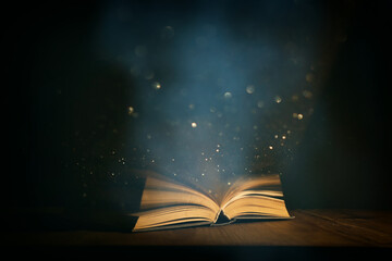 Magical image of open antique book over wooden table with glitter lights