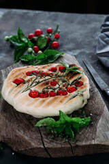 Focaccia with tomatoes and herbs on a wooden table