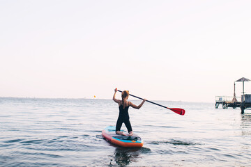 Close-up of a girl floating on a sup board. The concept of water sports, relaxation and self-immersion. Lonely woman alone on a board against a background of water and a pier.