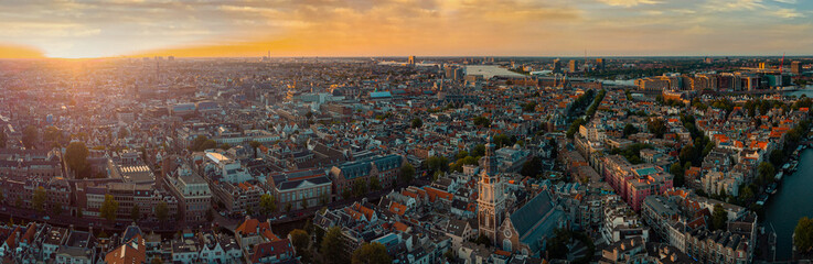 Obraz premium Beautiful evening panorama of Amstedam city looking towards the west with beautiful sunset and sun setting down over Amsterdam. Drone view.
