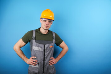 man wearing construction overalls and orange hard hat is on empty blue background