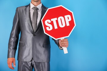  businessman holding a red stop sign on a blue background close-up. a person wearing a suit holds a sign with the words stop 
