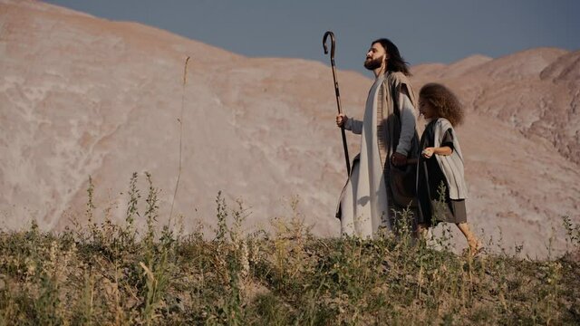 Jesus with a staff and children walks up the hill. The wind is blowing, the sun is shining. High quality 4k footage