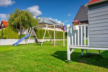 Green garden with a beautiful wooden house for children and a playground at summer.