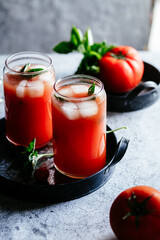 Tomato juice with ice in a glass on a gray background