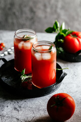 Tomato juice with ice in a glass on a gray background