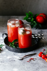 Tomato juice with ice in a glass on a gray background