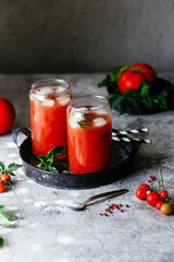 Tomato juice with ice in a glass on a gray background