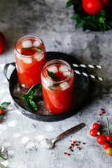 Tomato juice with ice in a glass on a gray background