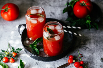 Tomato juice with ice in a glass on a gray background