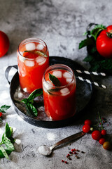 Tomato juice with ice in a glass on a gray background