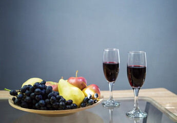 glasses with red wine on the table and a bowl with fruit grapes apple and pear