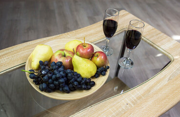 glasses with red wine on the table and a bowl with fruit grapes apple and pear