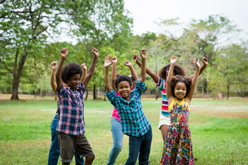 Group of African American children playing and raising their hands in the park. Cheerful diverse...