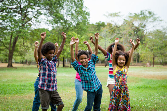 Group of African American children playing and raising their hands in the park. Cheerful diverse black children dancing together outdoor