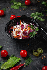 Delicious salad with white and red cabbage, carrots and fresh herbs, a fresh salad on the menu of a fast food restaurant on a dark stone table. Healthy option of fast food.