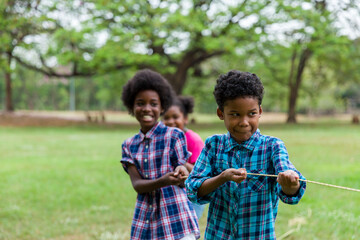 Group of African American boy and girl playing tug of war together in the park. Cheerful children...