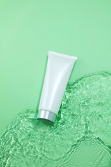 White bottle cosmetic tubes on the green water surface texture with ripples. Blank label for...