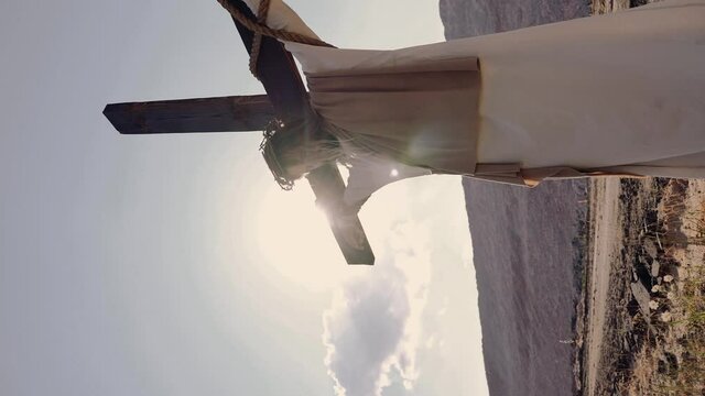 Jesus hangs on the cross, the wind is blowing, the sun is shining. Crucifixion. On the head is a wreath of thorns. Vertical video. High quality 4k footage